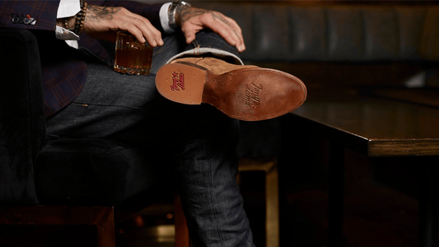 A man sitting in a room of whiskey barrels, wearing the Lenado in brown. 