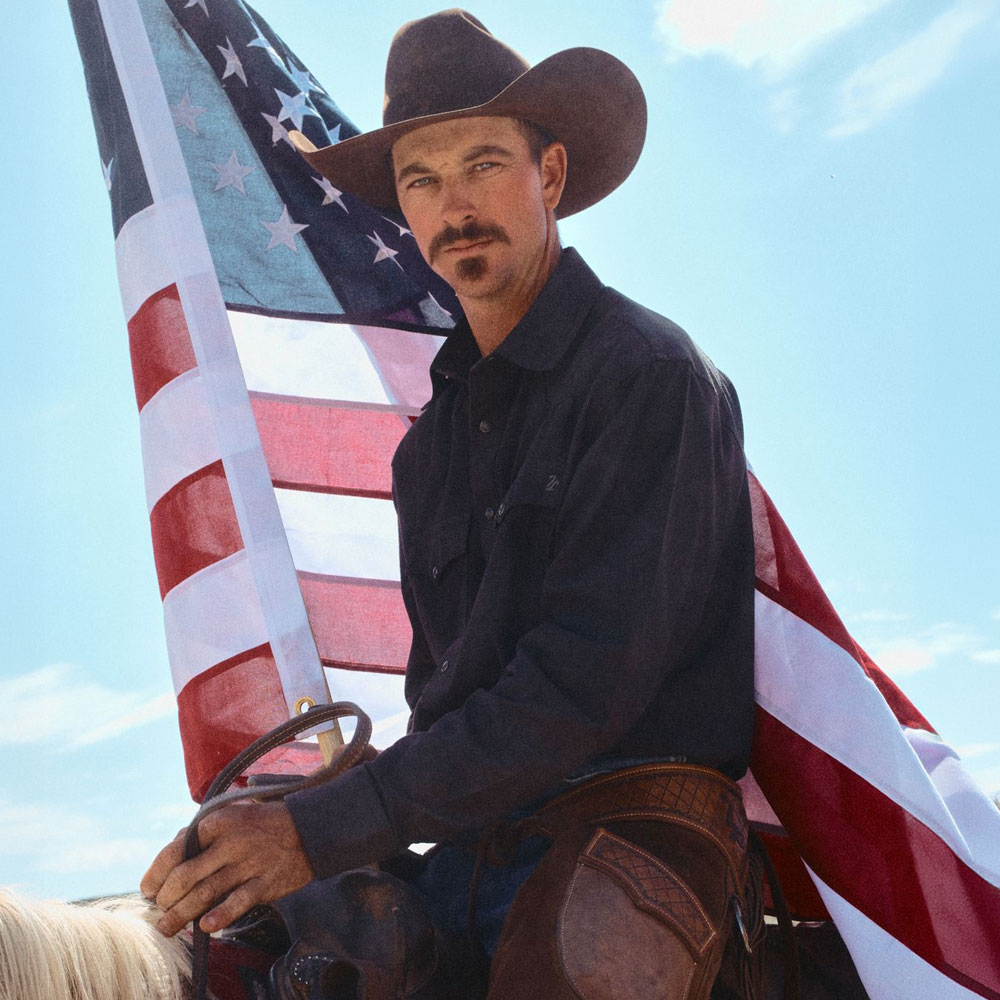 Man sitting on a horse with an American flag behind him.