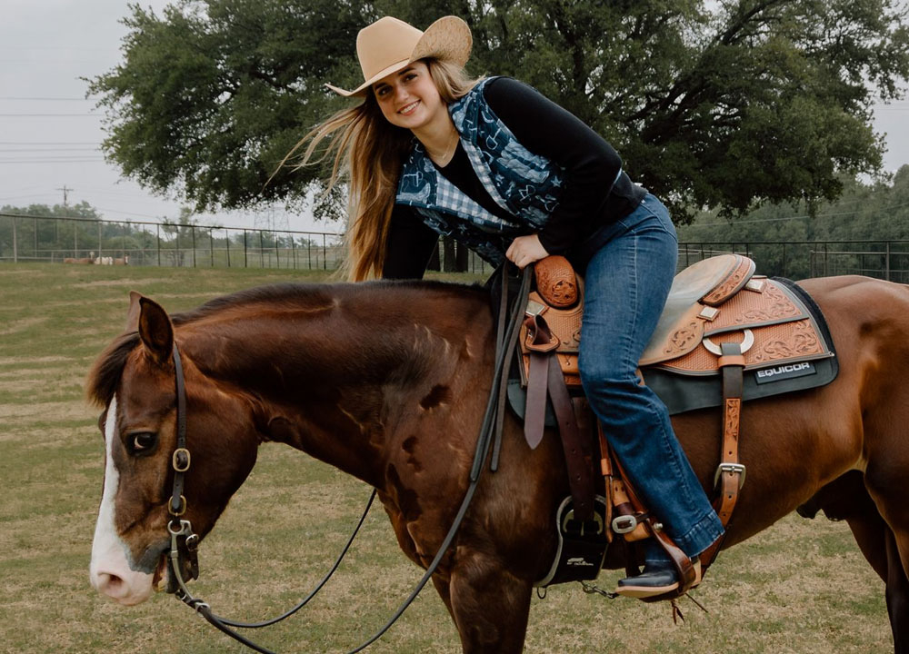 Harper de pie frente a una arena con un caballo marr&oacute;n.