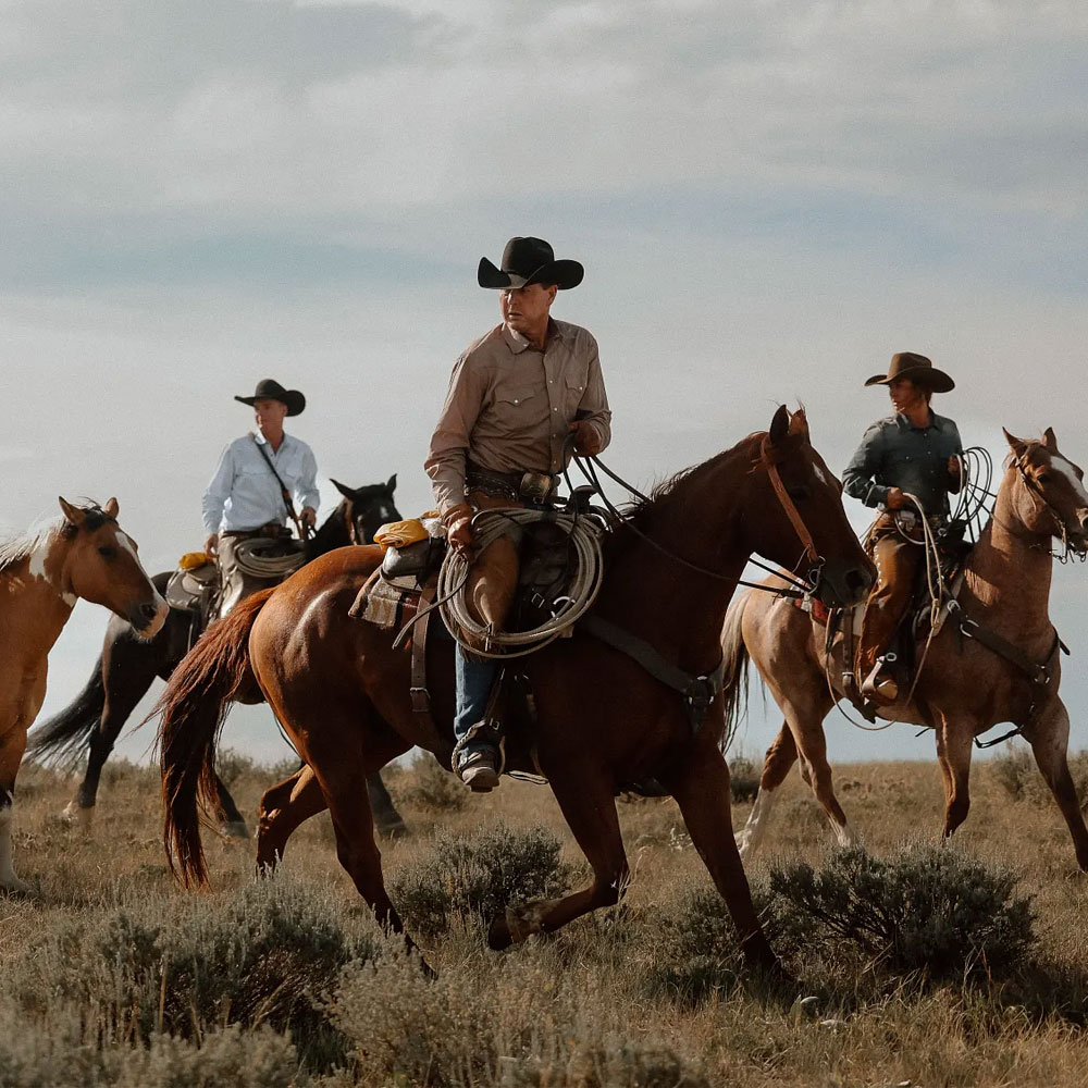 A group of cowboys riding horses wearing Tony Lama western boots.