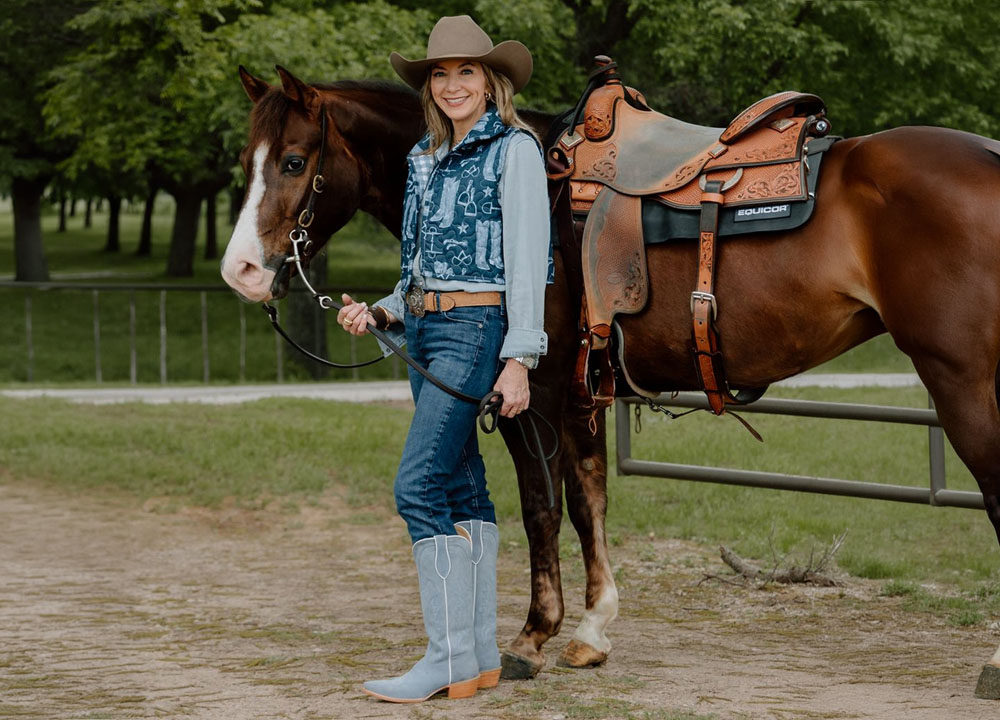 Kristen Kiseljack de pie junto a un caballo, luciendo un par de botas Ida Mae en color azul.