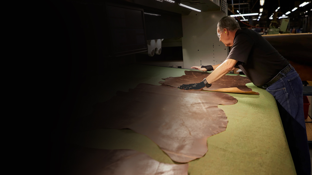 A factory worker spreads out leather on a table.