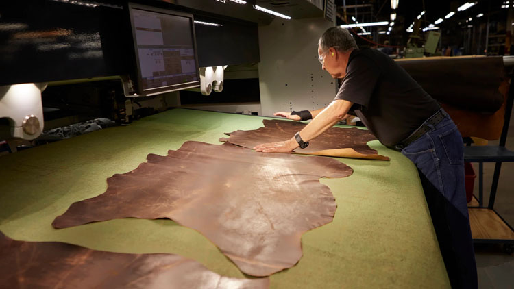 A factory worker spreads out leather on a table.