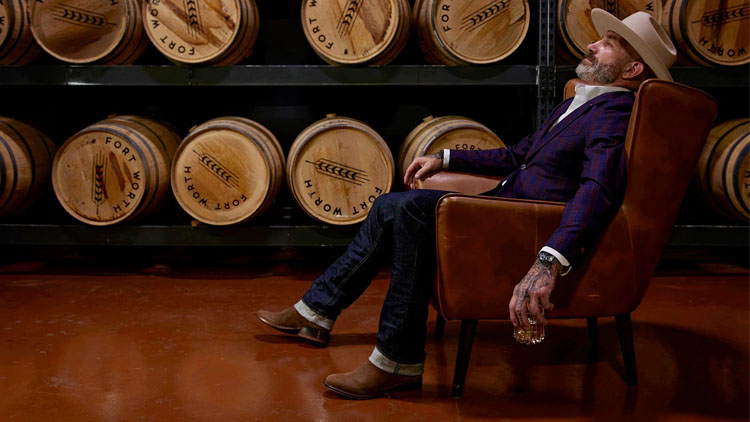 Man wearing a pair of roughout Derby boots in brown, sitting in a room full of whiskey barrels.