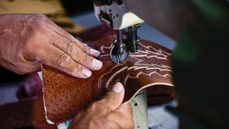Factory worker stitches thread into a Tony Lama boot.