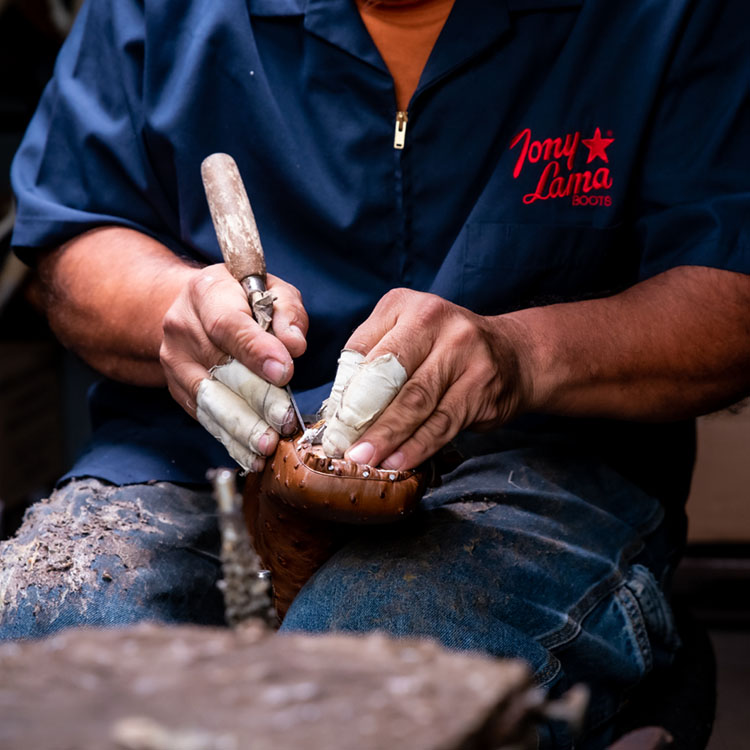 Man works on leather boots with tool. 