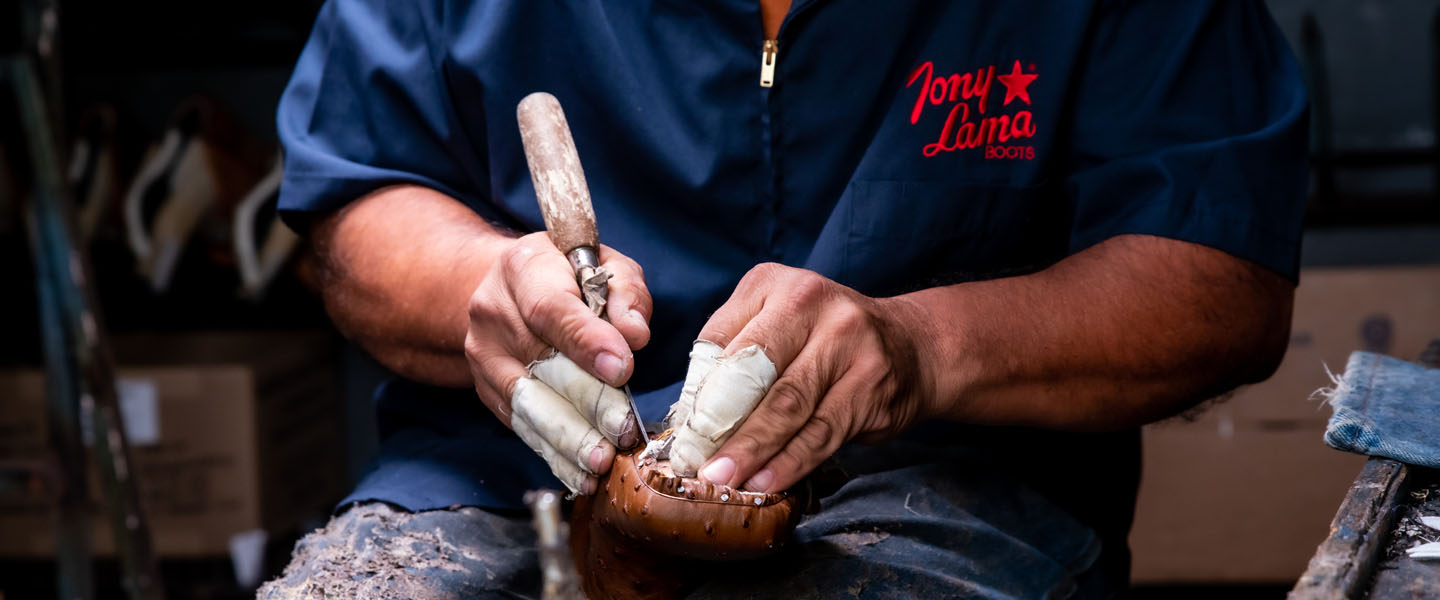 Man works on leather boots with tool. 