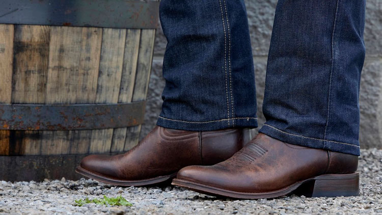 Man wearing a pair of roughout Derby boots in brown, standing next to a whiskey barrel.