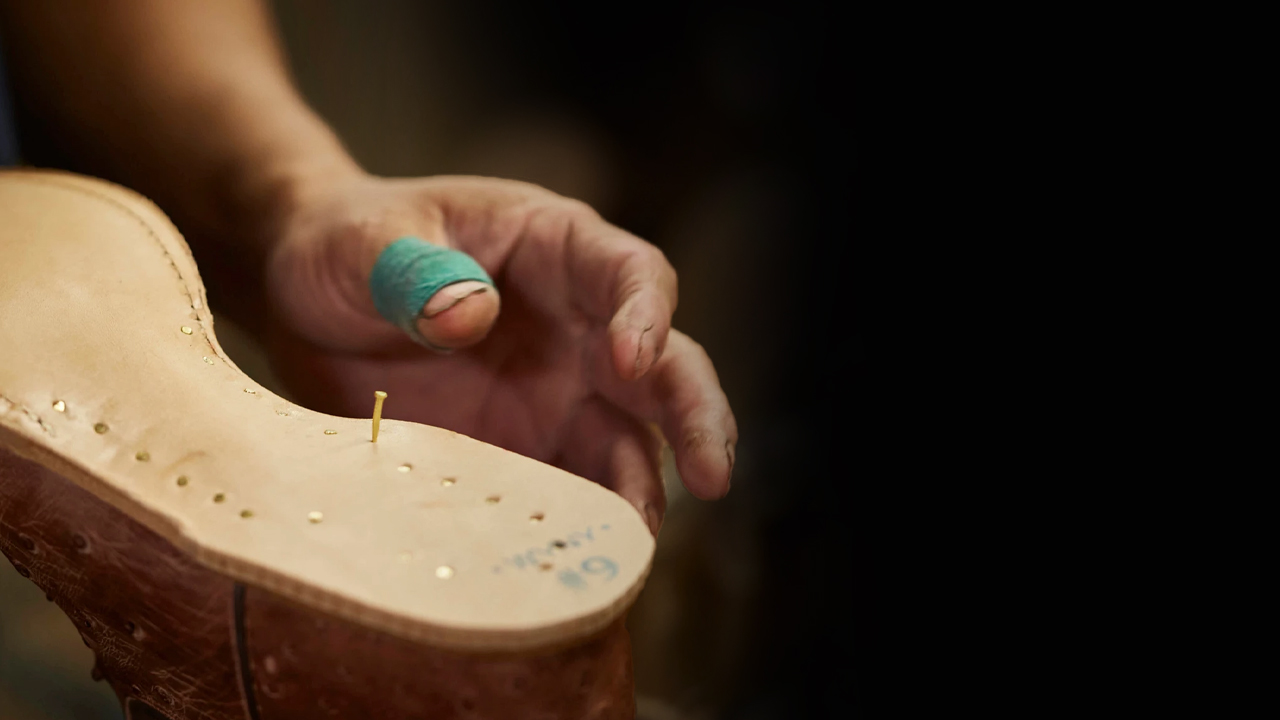 Factory worker hammers wooden pegs into a sole of a Tony Lama boot.