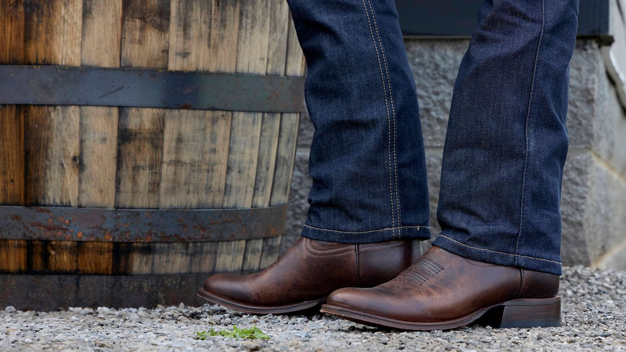 Hombre que llevaba un par de botas Derby de color marrón, de pie junto a un barril de whisky.