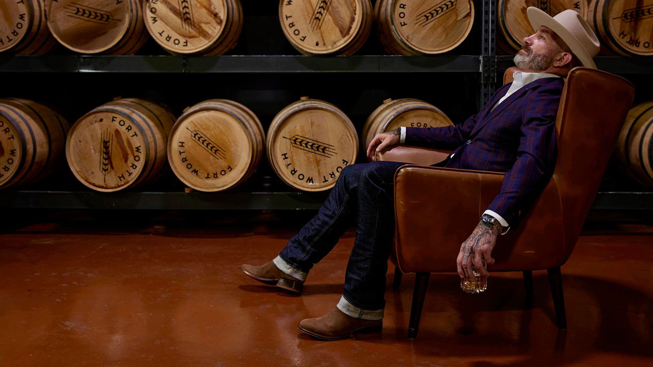 Man wearing a pair of roughout Derby boots in brown, sitting in a room full of whiskey barrels.