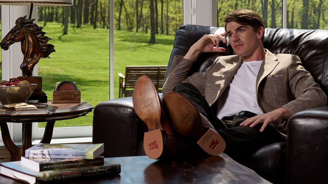 Image of man sitting on a leather chair with his legs up on a table wearing a pair of Tony Lama Derby Western boots.