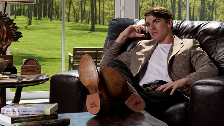 Image of man sitting on a leather chair with his legs up on a table wearing a pair of Tony Lama Derby Western boots.