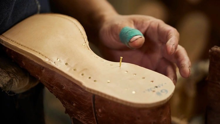 Factory worker hammers wooden pegs into a sole of a Tony Lama boot.