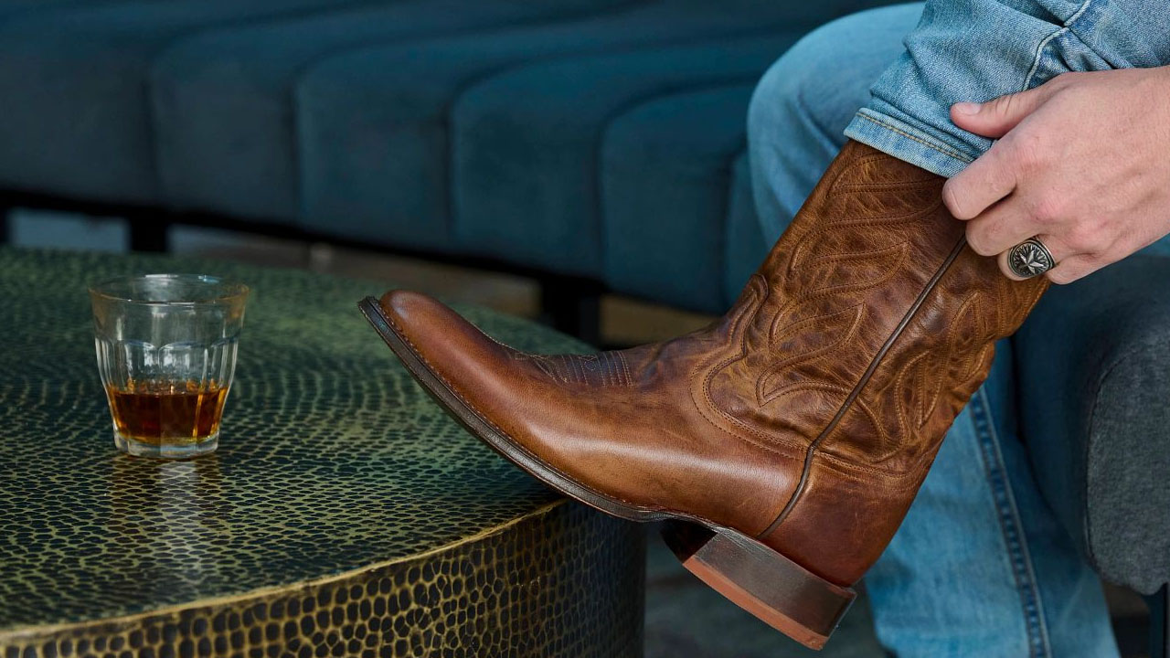Hombre que llevaba un par de botas Derby de color marrón con un vaso de whisky sobre una mesa de café.